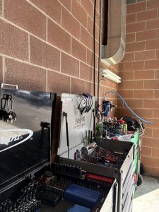 Seattle commercial exterminator in uniform inspecting a restaurant kitchen floor baseboard for odorous house ants and little black ants, with Space Needle visible through window